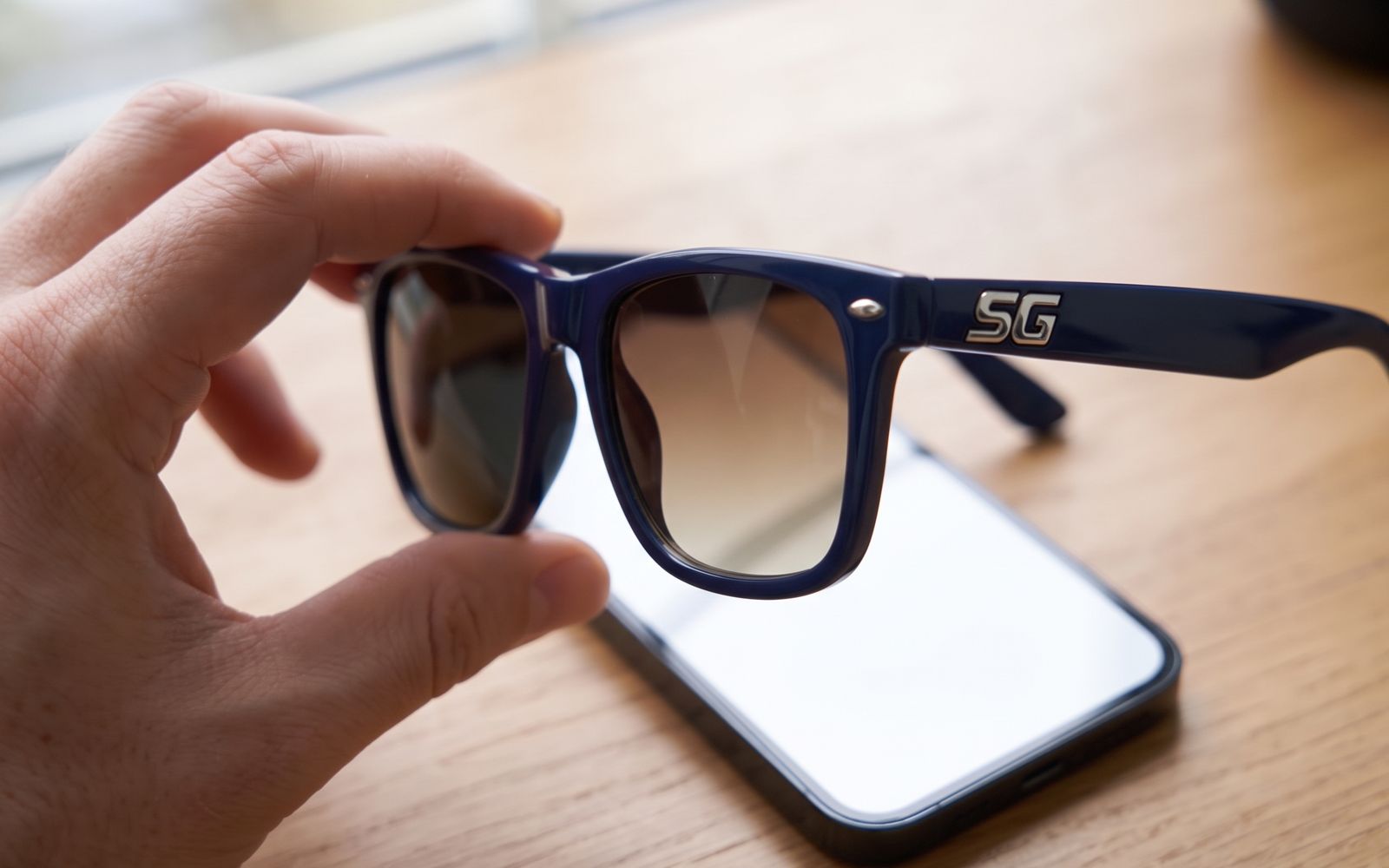 Une main tient la paire SG devant un écran de téléphone : à travers le verre, l'écran paraît noir